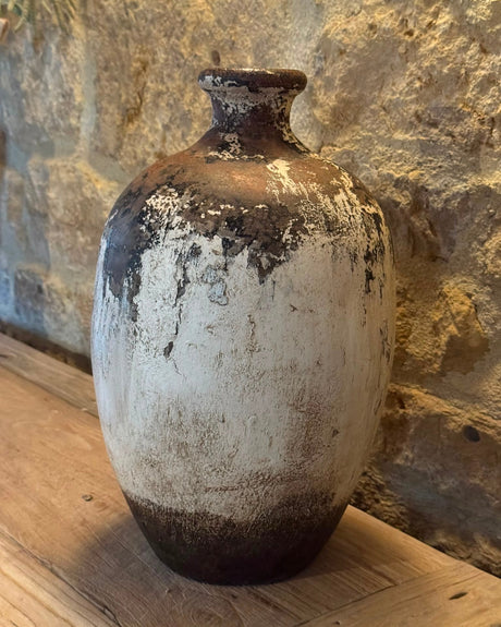 Vintage ceramic jar with a textured surface on a wooden surface against a stone wall.