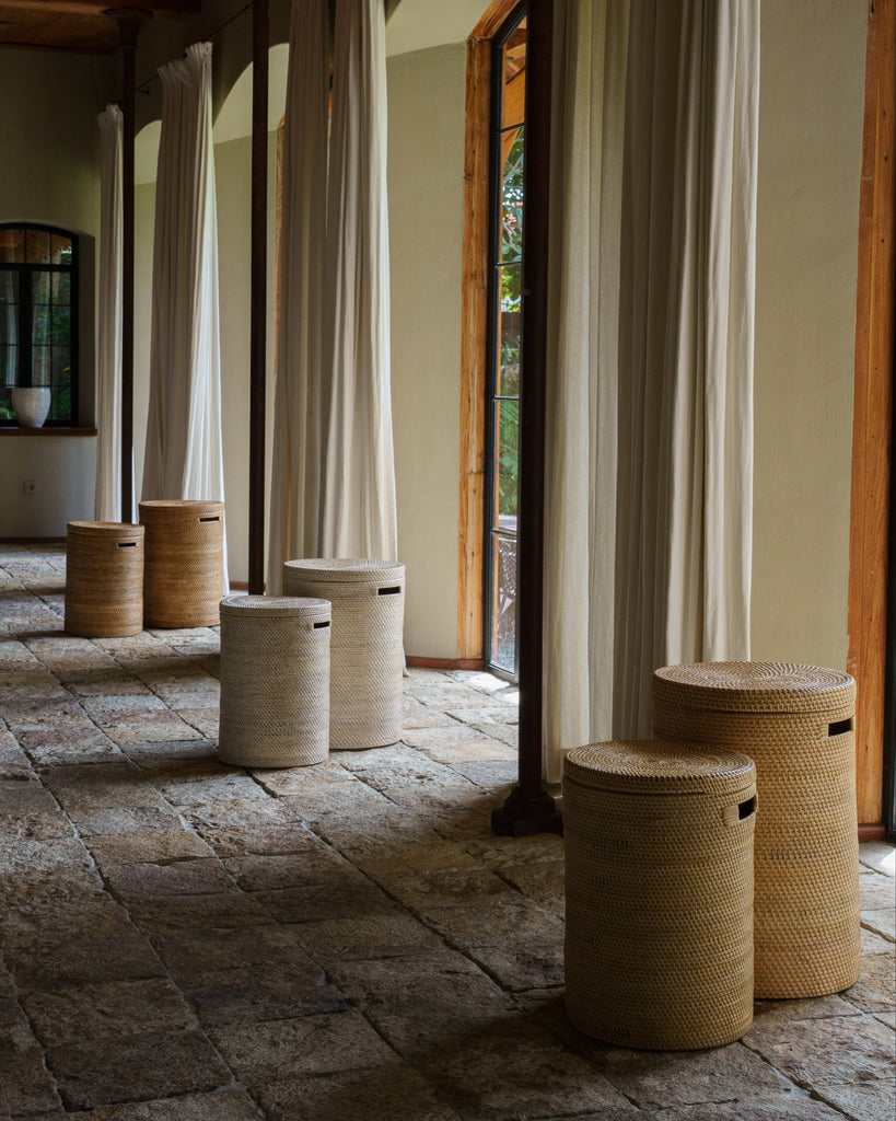 Woven cylindrical stools arranged in a room with stone flooring and large windows.