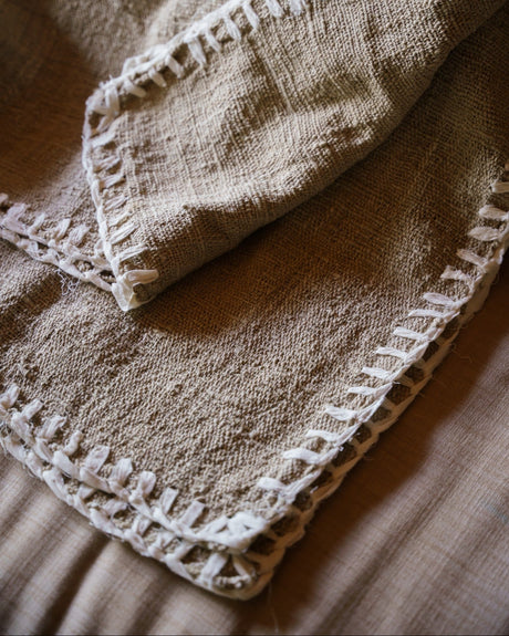 A light brown raw cotton hand woven throw with a textured pattern, draped over a couch