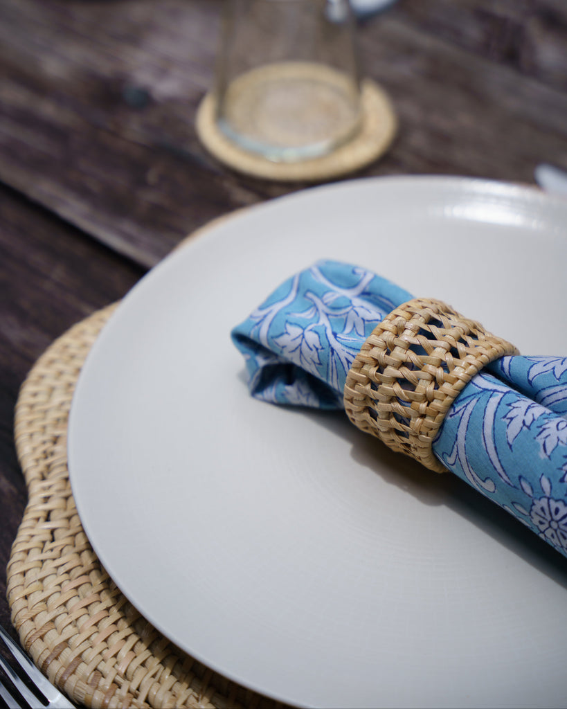 Napkin folded on a plate with a woven napkin ring on a wooden table.