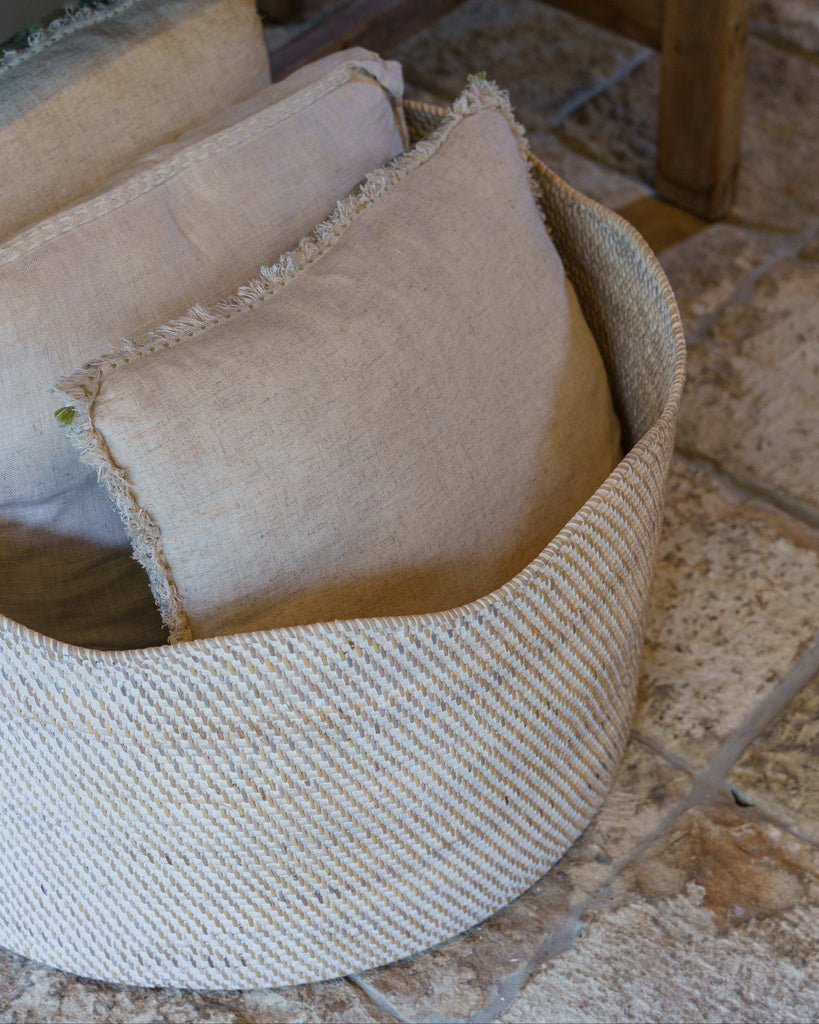 Beige textured pillows in a woven basket on a stone floor